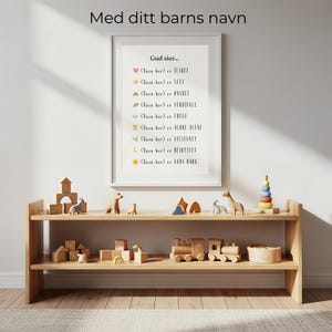 May include: A framed white wall art print featuring the text 'Gud sier...' followed by nine lines of Norwegian phrases starting with '(Navn her)' and ending with descriptive words, each preceded by a small colorful icon like a heart, star, or rainbow.