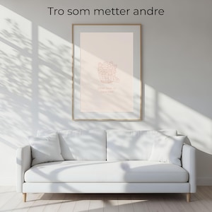 Könnte beinhalten: Ein gerahmter Kunstdruck mit einem hellbraunen Holzrahmen hängt an einer weißen Wand über einem weißen Sofa. Der Druck zeigt eine Strichzeichnung in hellbrauner Farbe mit Text oben und unten. Der Text oben lautet "Tro som metter andre".