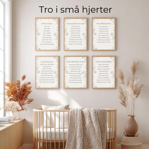 May include: A wall display of six framed prints with text and floral designs. The prints are in a nursery setting, above a wooden crib with a beige blanket. The text at the top reads "Tro i små hjerter".