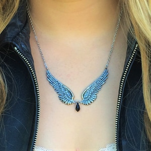 May include: A silver necklace with a pair of angel wings and a black crystal pendant.
