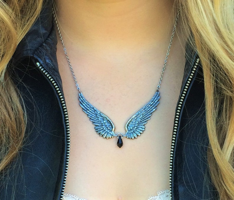 May include: A silver necklace with a pair of angel wings and a black crystal pendant.
