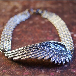 Puede incluir: Una pulsera de plata con un dise&ntilde;o de ala detallado. El ala est&aacute; hecha de m&uacute;ltiples capas de metal, creando un aspecto texturizado. La pulsera est&aacute; hecha de un estilo de cadena de eslabones.