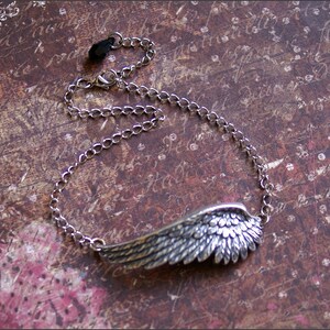 May include: A silver chain necklace with a detailed silver wing pendant. The chain has a black clasp.