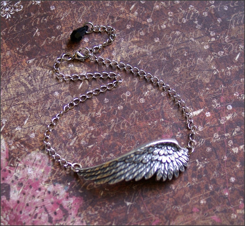 May include: A silver chain necklace with a detailed silver wing pendant. The chain has a black clasp.
