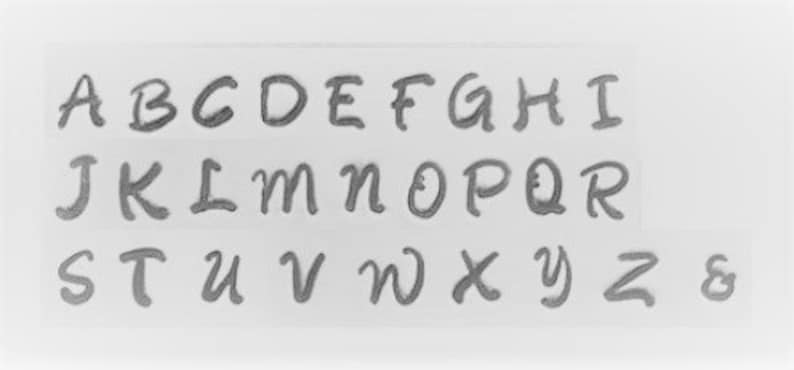 Puede incluir: Una imagen de primer plano de una tabla de fuentes que muestra el alfabeto en un estilo de escritura a mano. Las letras est&aacute;n en may&uacute;sculas y est&aacute;n escritas en una fuente cursiva. Las letras est&aacute;n dispuestas en tres filas. La primera fila muestra las letras A a I. La segunda fila muestra las letras J a R. La tercera fila muestra las letras S a Z y el s&iacute;mbolo de ampersand.