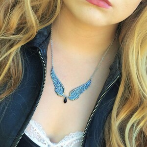 May include: A silver necklace with a pendant featuring a pair of blue angel wings with a black gemstone drop.