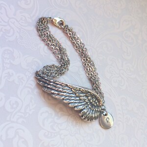 Puede incluir: Pulsera de plata con un dije de ala de &aacute;ngel detallado y un peque&ntilde;o dije con la letra 'R' colgando.