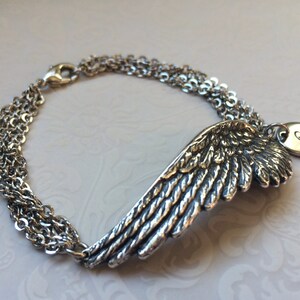 Puede incluir: Pulsera de plata con un dije de ala detallada y un dije redondo con la letra "R" grabada.