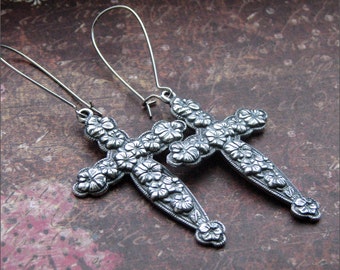 May include: A pair of silver earrings with a cross design. The cross is decorated with floral details.