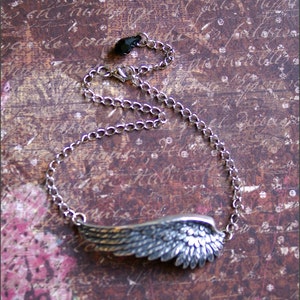 May include: A silver chain necklace with a detailed silver wing pendant. The chain is a simple curb chain style.