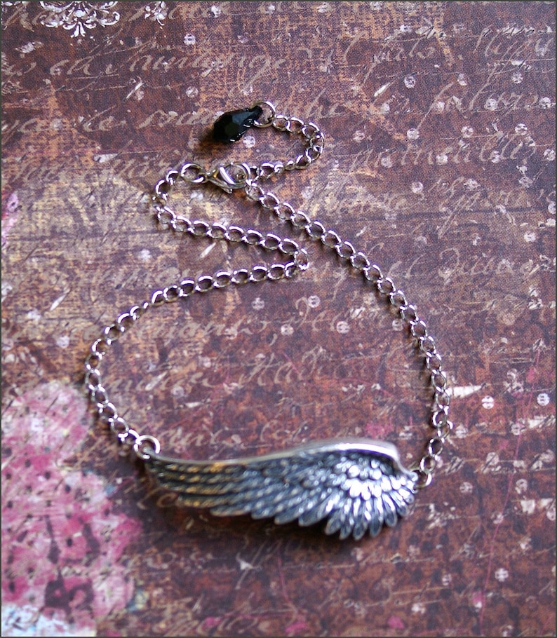 May include: A silver chain necklace with a detailed silver wing pendant. The chain is a simple curb chain style.