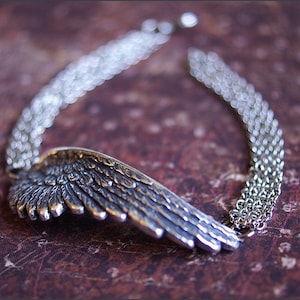 May include: A silver necklace with a detailed wing pendant and a chain made of multiple strands.
