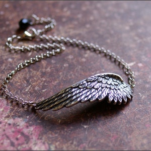 May include: A silver chain bracelet with a detailed silver wing pendant. The chain has a black bead at the clasp.