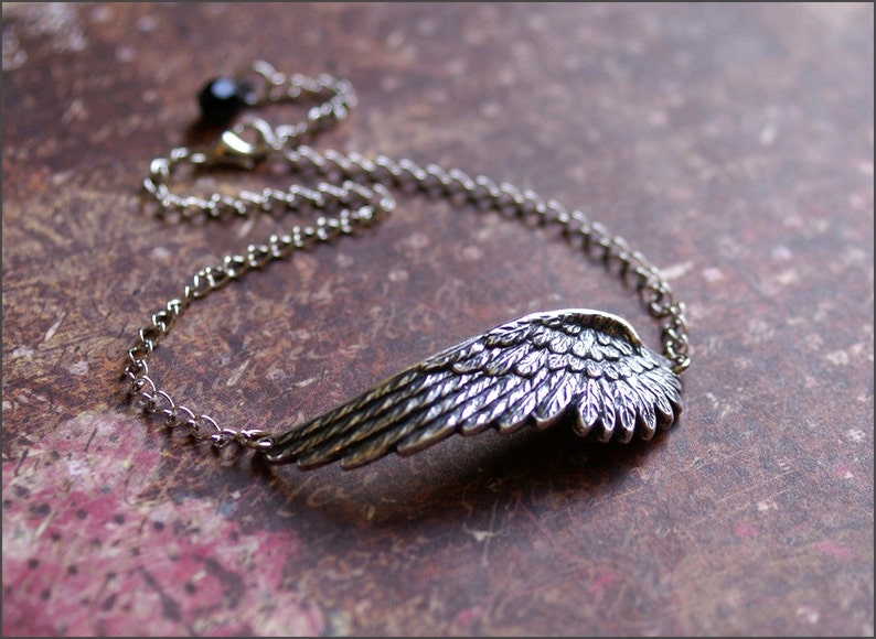 May include: A silver chain bracelet with a detailed silver wing pendant. The chain has a black bead at the clasp.