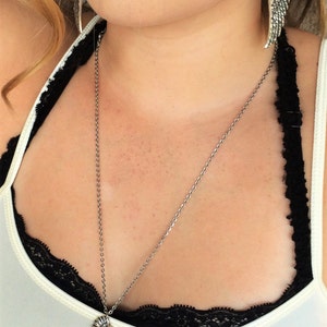 May include: A silver necklace with a wing pendant. The necklace is worn by a person with a white tank top and black lace trim.