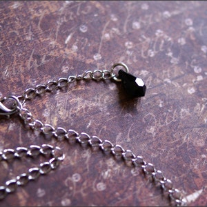 May include: A silver chain necklace with a black teardrop-shaped crystal pendant.