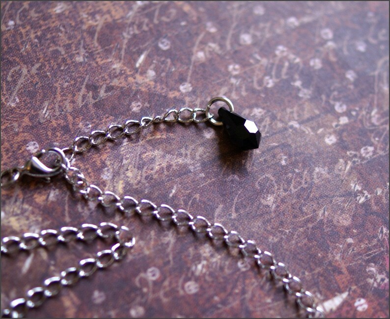 May include: A silver chain necklace with a black teardrop-shaped crystal pendant.