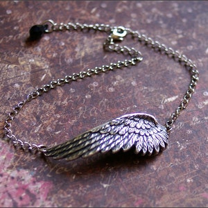 May include: A silver chain bracelet with a detailed silver wing charm. The wing is textured and has a feathered design.
