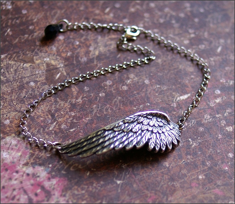 May include: A silver chain bracelet with a detailed silver wing charm. The wing is textured and has a feathered design.