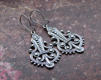 Peut inclure: Une paire de boucles d'oreilles en filigrane argentées avec un design délicat et complexe. Les boucles d'oreilles sont en métal et ont une finition brillante.