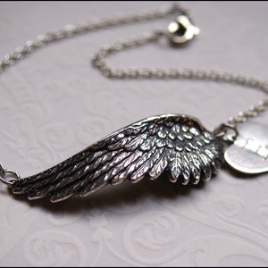 Può includere: Un braccialetto con catena d'argento con un ciondolo a forma di ala d'argento dettagliato e un ciondolo a forma di cuore con la lettera "E" incisa.