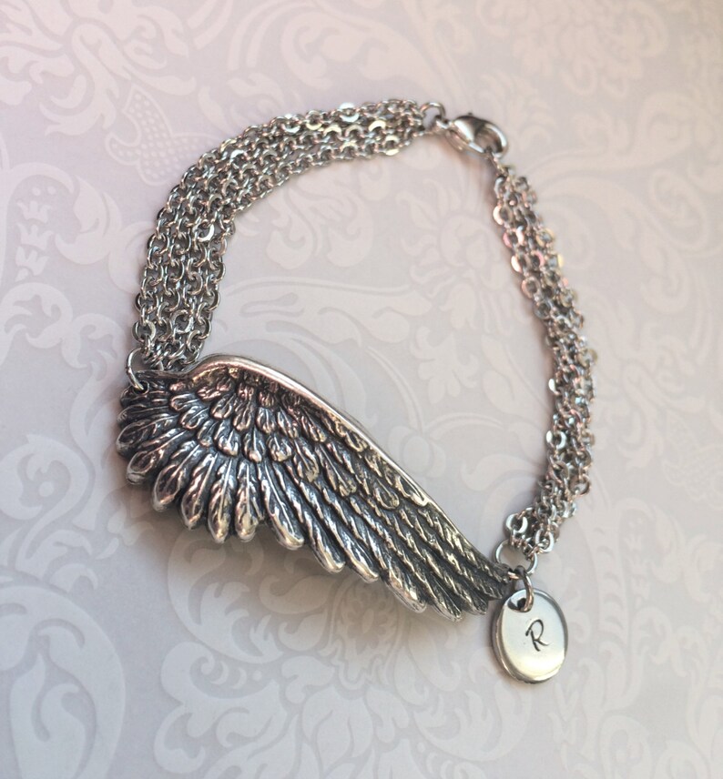 May include: Silver charm bracelet with a detailed angel wing charm and a round charm with the letter "R" engraved on it.
