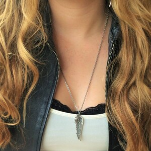 May include: A silver necklace with a detailed wing pendant. The necklace is worn by a person with long blonde hair and a black leather jacket.