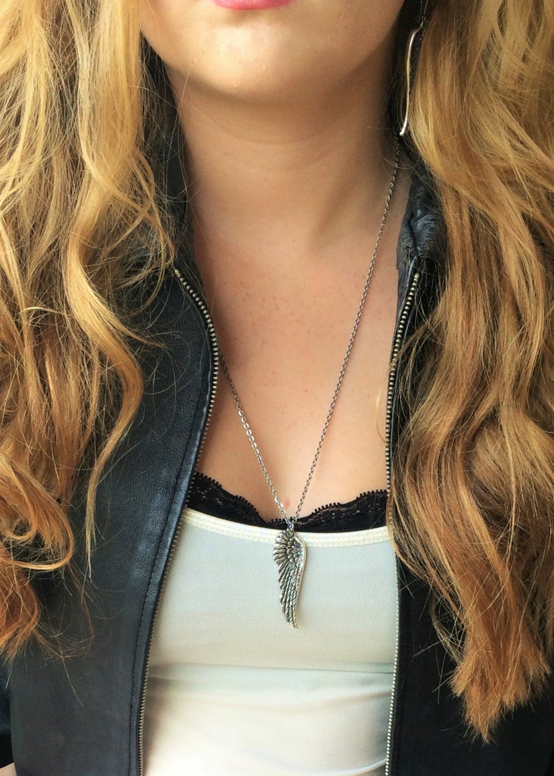 May include: A silver necklace with a detailed wing pendant. The necklace is worn by a person with long blonde hair and a black leather jacket.