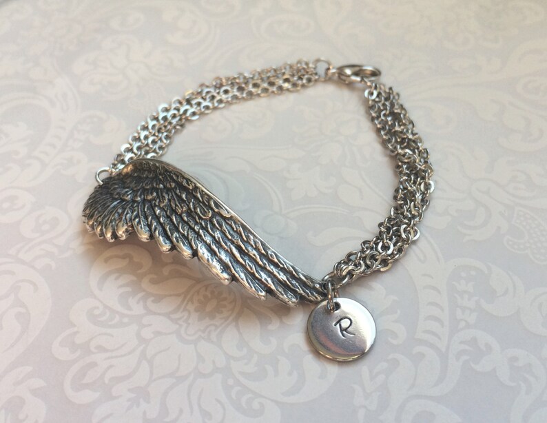 May include: Silver bracelet with a single wing charm and a round charm with the letter "R" engraved on it.