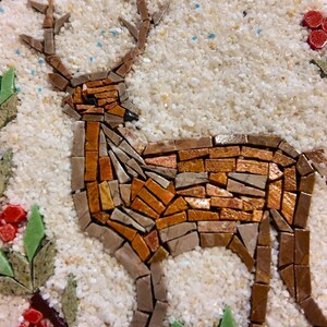 May include: A mosaic deer with brown and orange tones stands on a white, textured background, surrounded by green leaves and red berries. The artwork is set within a round, wooden frame, creating a rustic, nature-inspired design.