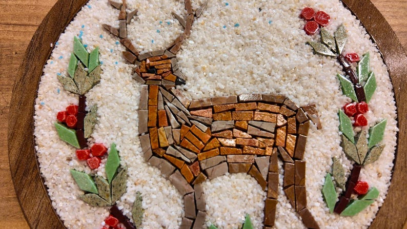 May include: A mosaic deer with brown and orange tones stands on a white, textured background, surrounded by green leaves and red berries. The artwork is set within a round, wooden frame, creating a rustic, nature-inspired design.