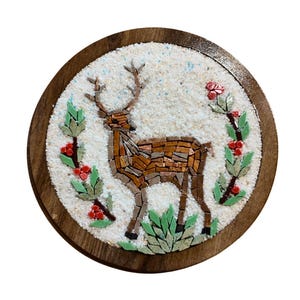 May include: Round wooden mosaic featuring a deer with antlers, crafted from brown and tan tiles. The deer is surrounded by green leaves and red berries on a white background, set within a dark brown wooden frame.