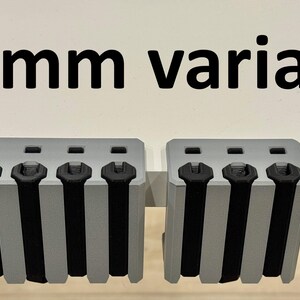 K&ouml;nnte beinhalten: Drei graue, rechteckige Objekte mit schwarzen Akzenten und vertikalen schwarzen Streifen. Der Text "50mm variant" befindet sich &uuml;ber den Objekten. Die Objekte scheinen eine Art Hardware oder Komponente zu sein.