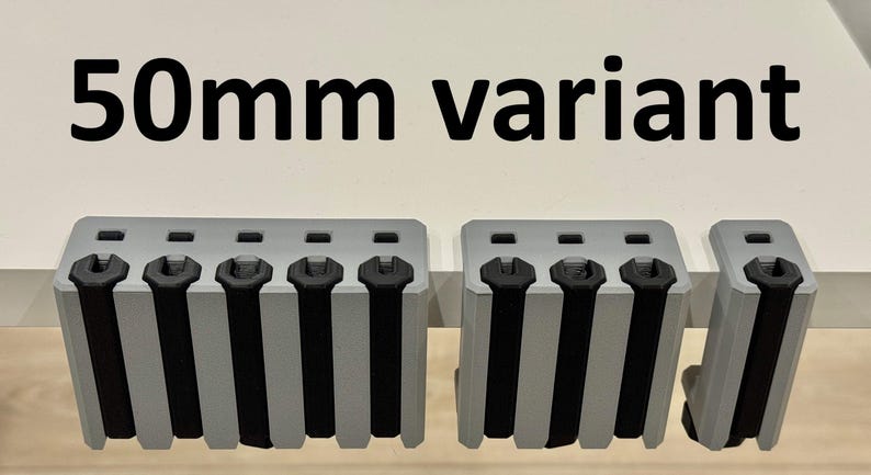 K&ouml;nnte beinhalten: Drei graue, rechteckige Objekte mit schwarzen Akzenten und vertikalen schwarzen Streifen. Der Text "50mm variant" befindet sich &uuml;ber den Objekten. Die Objekte scheinen eine Art Hardware oder Komponente zu sein.