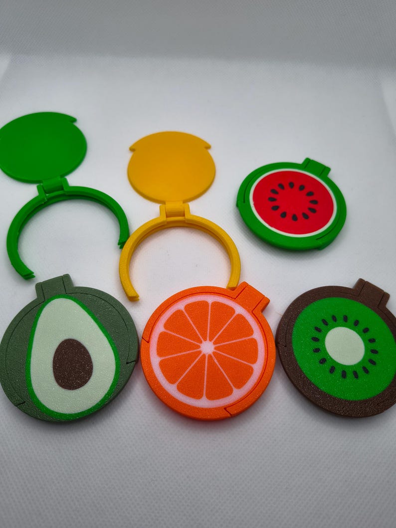 May include: A selection of fruit-shaped bottle stoppers. The stoppers are designed as a watermelon, orange, kiwi, and avocado. Each stopper has a hinged lid and a ring for attaching to a bottle. The colours include green, red, yellow, and brown.