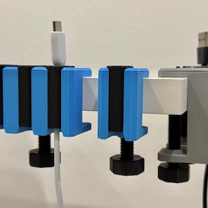 K&ouml;nnte beinhalten: Blaue und schwarze Kabelorganisatoren, an einer wei&szlig;en Stange befestigt. Die Organizer haben einen Schraubmechanismus. Ein wei&szlig;es USB-C-Kabel und ein schwarzes USB-Kabel sind eingesteckt.