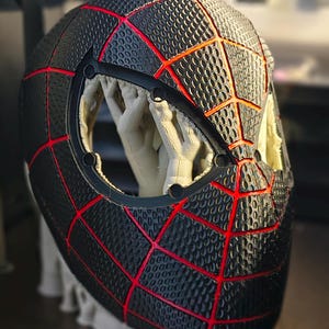 May include: Black and red Spider-Man mask with a textured surface and a web-like design. The mask features a large eye opening and is likely a cosplay or costume accessory.