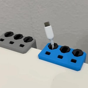 K&ouml;nnte beinhalten: Zwei Kabelorganisatoren, einer grau und einer blau, liegen auf einer wei&szlig;en Oberfl&auml;che. Der blaue Organizer h&auml;lt ein wei&szlig;es USB-C-Kabel. Jeder Organizer hat drei kreisf&ouml;rmige Schlitze und mehrere kleinere rechteckige Schlitze.