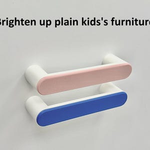 Könnte beinhalten: Zwei weiße Schrankgriffe mit abgerundeten Enden. Einer hat eine rosa Mitte, der andere eine blaue Mitte. Der Text "Brighten up plain kids's furniture" befindet sich oben im Bild.