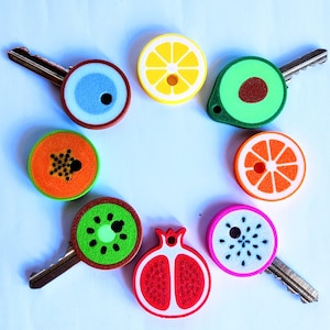 May include: A collection of decorative key covers in various fruit designs, including a lemon, avocado, orange slice, kiwi, and pomegranate. Each cover is brightly colored and attached to a silver key, creating a fun and functional accessory.