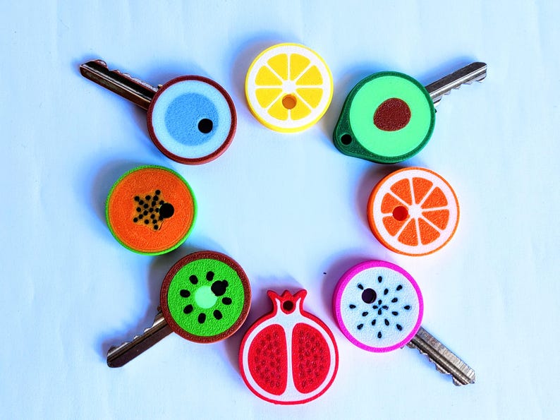 May include: A collection of decorative key covers in various fruit designs, including a lemon, avocado, orange slice, kiwi, and pomegranate. Each cover is brightly colored and attached to a metal key, creating a fun and functional accessory.