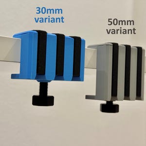 K&ouml;nnte beinhalten: Zwei Klemmenvarianten werden gezeigt: eine blaue 30-mm-Klemme und eine graue 50-mm-Klemme. Beide Klemmen haben schwarze Gummipads und eine schwarze Stellschraube. Der Text "30mm variant" und "50mm variant" ist sichtbar.