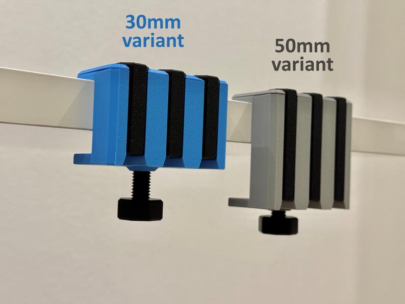 K&ouml;nnte beinhalten: Zwei Klemmenvarianten werden gezeigt: eine blaue 30-mm-Klemme und eine graue 50-mm-Klemme. Beide Klemmen haben schwarze Gummipads und eine schwarze Stellschraube. Der Text "30mm variant" und "50mm variant" ist sichtbar.