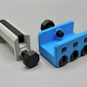 K&ouml;nnte beinhalten: Zwei 3D-gedruckte Klemmen. Eine ist hellgrau mit einem schwarzen Griff und einer schwarzen Schraube. Die andere ist blau mit schwarzen Schrauben. Die Klemmen sind zum Festhalten von Objekten konzipiert.