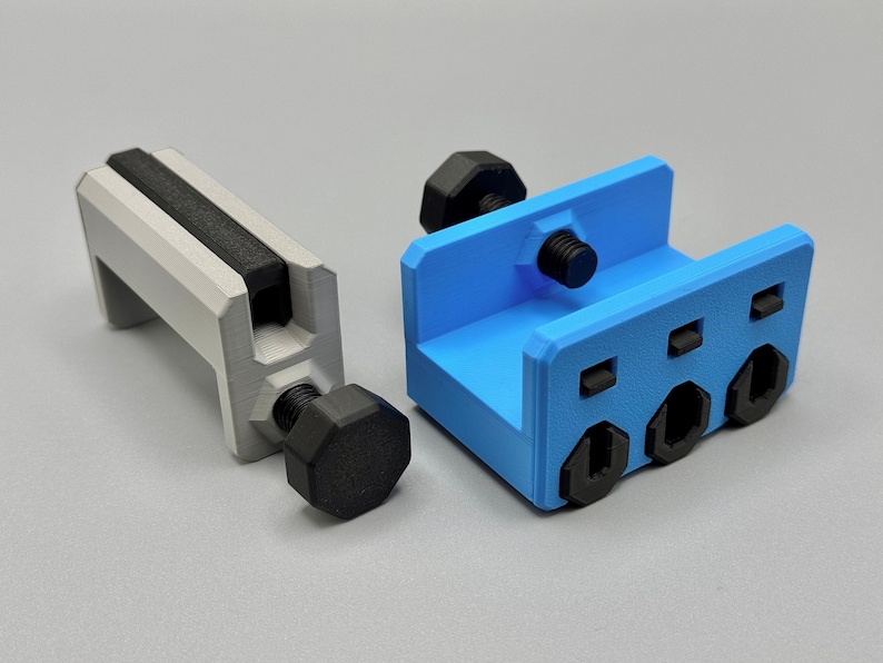 K&ouml;nnte beinhalten: Zwei 3D-gedruckte Klemmen. Eine ist hellgrau mit einem schwarzen Griff und einer schwarzen Schraube. Die andere ist blau mit schwarzen Schrauben. Die Klemmen sind zum Festhalten von Objekten konzipiert.