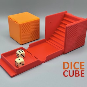 Puede incluir: Un cubo de dados naranja y rojo con un diseño texturizado. El cubo está abierto, revelando una escalera y una bandeja con dos dados. El texto "DICE CUBE" se muestra en naranja y rojo.