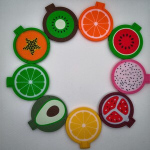 May include: A selection of fruit-shaped coasters featuring designs of kiwi, orange, watermelon, lime, avocado, lemon, papaya, dragon fruit, and pomegranate. Each coaster has a circular design with a fruit slice illustration and a small tab.