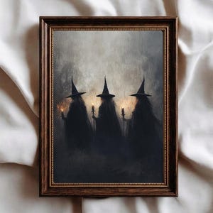 May include: A framed wall art print featuring three dark, cloaked figures wearing pointed hats, each holding a small glowing candle. The artwork is set against a misty, grey background and is enclosed in a dark brown, ornate wooden frame.
