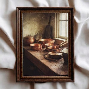 Puede incluir: Una impresión enmarcada que presenta una naturaleza muerta de utensilios de cocina de cobre. La imagen muestra varias ollas y sartenes dispuestas sobre una superficie de madera rústica cerca de una ventana. Los tonos cálidos del cobre contrastan con el marco de madera oscura y el fondo apagado.