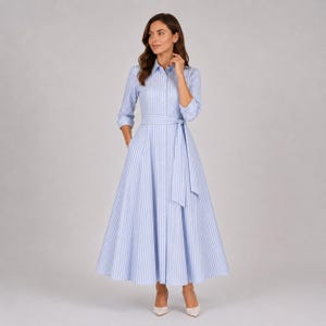 May include: A long-sleeved shirt dress featuring a light blue and white vertical striped pattern. The dress has a collared neckline, a button-down front, and a matching fabric tie belt at the waist, with a full, flared skirt that reaches the ankles.